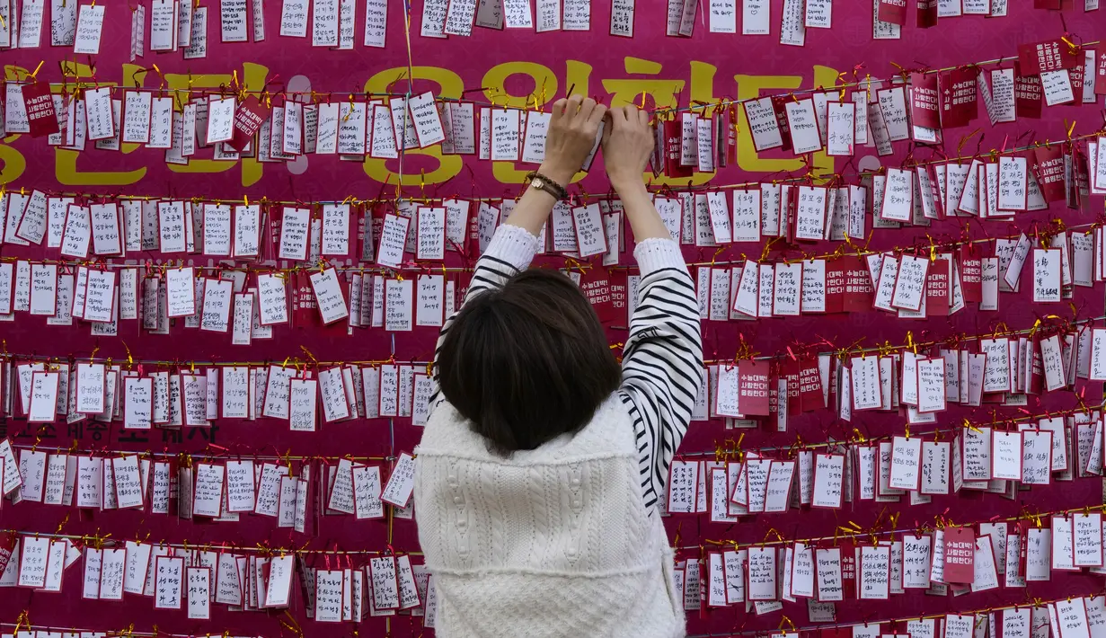 Seorang wanita menggantungkan kertas untuk mendoakan keberhasilan anaknya dalam ujian masuk perguruan tinggi di kuil Buddha Jogyesa, Seoul, Rabu (17/11/2021). Sekitar 500.000 siswa SMA di Korea Selatan diperkirakan akan mengikuti Tes Kemampuan Skolastik Perguruan Tinggi. (AP Photo/Ahn Young-joon)