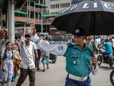 Seorang petugas polisi Bangladesh memegang payung untuk melindungi dirinya dari sengatan matahari saat mengatur lalu lintas di persimpangan jalan di Dhaka pada tanggal 12 Agustus 2024. (LUIS TATO/AFP)