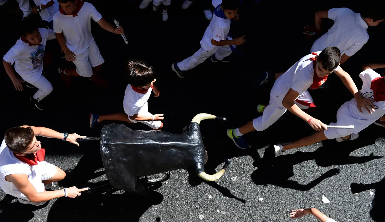 Seorang pria mendorong banteng mainan untuk mengejar anak-anak saat Encierro Txiki selama Festival San Fermin di Pamplona, Spanyol (13/7). (AFP Photo/Ander Gillenea)