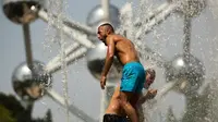 Dua pria mendinginkan diri dengan bermain di air mancur umum dekat Atomium saat gelombang panas melanda Eropa di Brussels, Belgia, Rabu (24/7/2019). Warga turun ke air mancur saat gelombang panas yang memecahkan rekor melanda Eropa. (AP Photo/Francisco Seco)