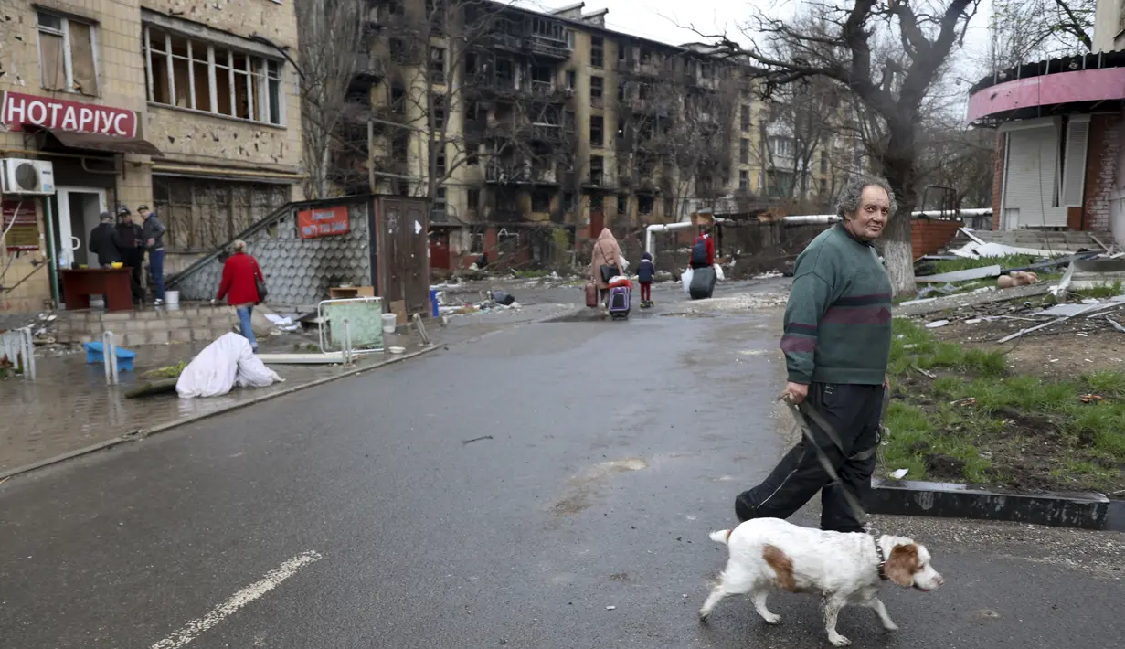 Seorang pria dengan seekor anjing berjalan di jalan yang rusak selama pertempuran sengit di gedung apartemen di daerah yang dikendalikan oleh pasukan separatis yang didukung Rusia di Mariupol, Ukraina, Selasa (19/4/2022).  (AP Photo/Alexei Alexandrov)