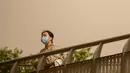 Seorang wanita yang memakai masker wajah berdiri di jembatan penyeberangan saat badai pasir di Beijing, China, Kamis (6/5/2021). Debu dan badai pasir akhir musim semi mengirim indeks kualitas udara melonjak di Ibu Kota China pada hari ini. (AP Photo/Mark Schiefelbein