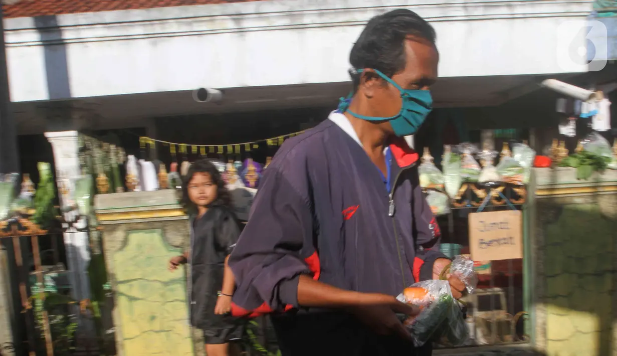 Seorang pria membawa sekantong sayuran yang digantung pada pagar rumah di Gang Palautan, Cilodong, Depok, Jumat (21/1/2022). Warga Rt 04 Rw 01 di kawasan tersebut secara swadaya berbagi sayuran, beras, dan bumbu masak secara gratis setiap hari Jumat.  (Liputan6.com/Herman Zakharia)