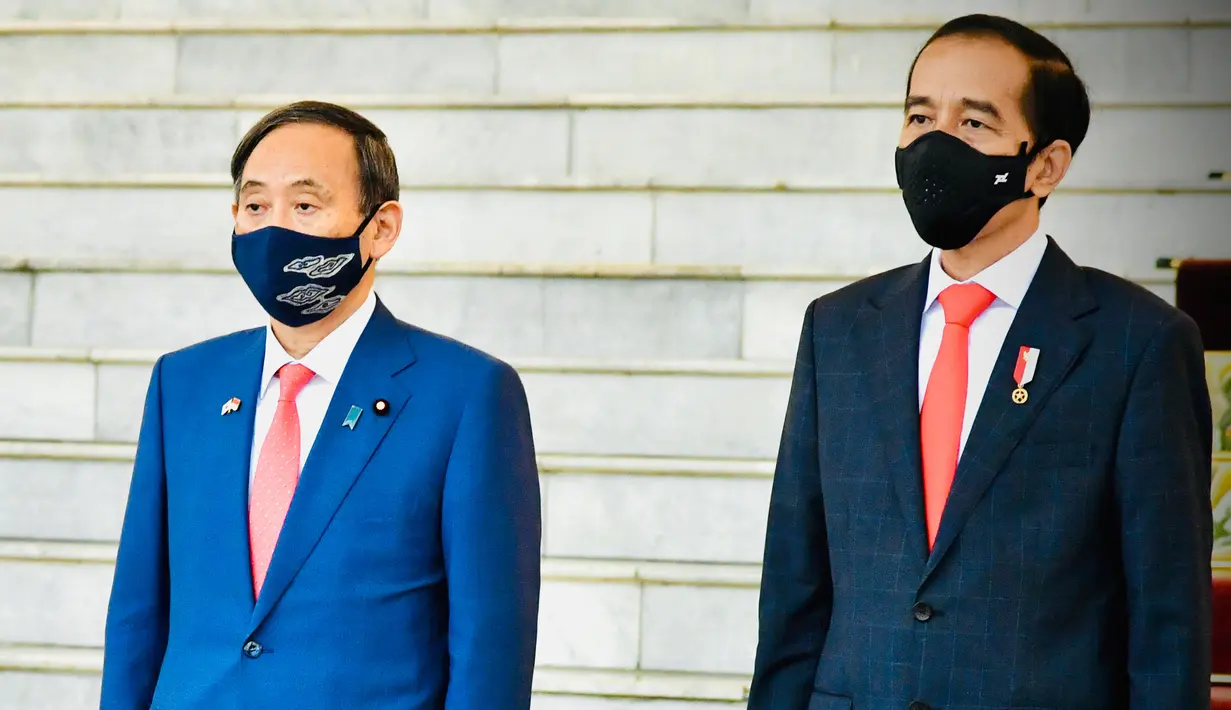 Presiden Joko Widodo bersama Perdana Menteri Jepang Yoshihide Suga (kiri), sama-sama mengenakan masker sebagai upaya mencegah penyebaran Covid-19, mendengarkan lagu kebangsaan saat upacara penyambutan di Istana Bogor, 20 Oktober 2020. (Laily Rachev/Indonesian Presidential Palace via AP)