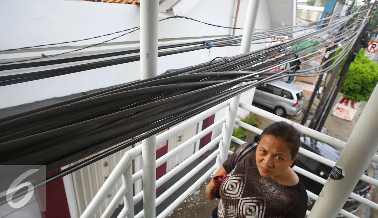 Warga melintas di bawah instalasi kabel yang menjuntai di JPO kawasan Cawang, Jakarta, Rabu (25/1). Selain mengganggu kenyamanan, buruknya penempatan instalasi kabel tersebut juga berbahaya bagi keselamatan pengguna JPO. (Liputan6.com/Immanuel Antonius)