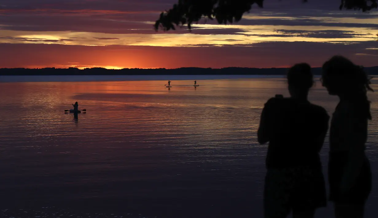 Orang-orang menikmati matahari terbenam di danau Chiemsee di Chieming, Jerman, Selasa, (25/8/2020).  Danau yang terletak di dekat kota Rosenheim ini sering diberi julukan "Laut Bayern'. (AP Photo / Matthias Schrader)