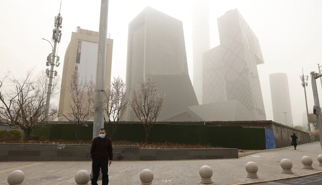 Seorang pria menunggu untuk menyeberang jalan dekat gedung pencakar langit saat badai pasir di Beijing (28/3/2021). Sebelumnya Badai pasir menyapu Beijing, China pada Senin (15/3/2021) pagi.  (AP Photo/Ng Han Guan)