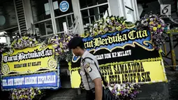 Anggota kepolisian melintas dekat karangan bunga di dekat lokasi ledakan bom, Terminal Kampung Melayu, Kamis (25/5). Karangan bunga itu tanda duka cita pihak kepolisian terhadap tiga polisi yang gugur dan para korban luka. (Liputan6.com/Faizal Fanani)