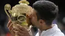 Petenis Serbia, Novak Djokovic cium Piala Wimbledon usai kalahkan petenis Italia, Matteo Berrettini di partai puncak tunggal putra. Kemenangan ini mengantarkan Djokovic menyamai rekor Nadal dan Federer sebagai petenis yang mampu mendapatkan 20 gelar Grand Slam. (Foto: AP/Kirsty Wigglesworth)