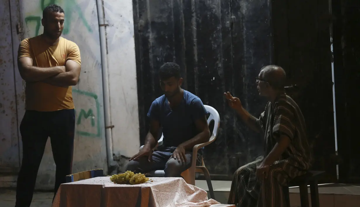 Seorang penjual anggur (tengah) menunggu pelanggan, sementara yang lain mengobrol dengannya selama penguncian yang diberlakukan selama pandemi virus corona, di kamp pengungsi Shati, di Kota Gaza, Selasa, (1/9/2020). (AP Photo/Adel Hana)