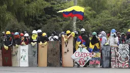 Pengunjuk rasa berdiri dengan perisai sambil mengibarkan bendera Kolombia di sekitar barikade yang terbakar selama protes anti-pemerintah di Bogota (28/5/2021). Warga Kolombia telah turun ke jalan selama berminggu-minggu setelah pemerintah mengusulkan kenaikan pajak. (AP Photo/Ivan Valencia)