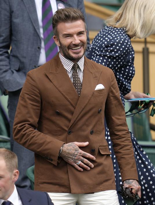 <p>David Beckham bersiap menyaksikan Simona Halep dari Rumania dan Amanda Anisimova dari AS bertanding pada hari kesepuluh Kejuaraan Wimbledon 2022 di The Klub Tenis All England, London (6/7/2022). Becks tampil keren mengenakan setelan jas cokelat di atas kemeja bergaris dan dasi berbintik dengan celana panjang putih ketat. (AP Photo/Kirsty Wigglesworth)</p>