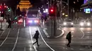Para komuter menyeberang jalan selama aturan jam malam di Melbourne, pada Selasa (17/8/2021). Kota terbesar kedua di Australia itu memberlakukan pembatasan tinggal di rumah pada pukul 9 malam hingga 5 pagi untuK meredam lonjakan Covid-19 varian Delta. (William WEST/AFP)