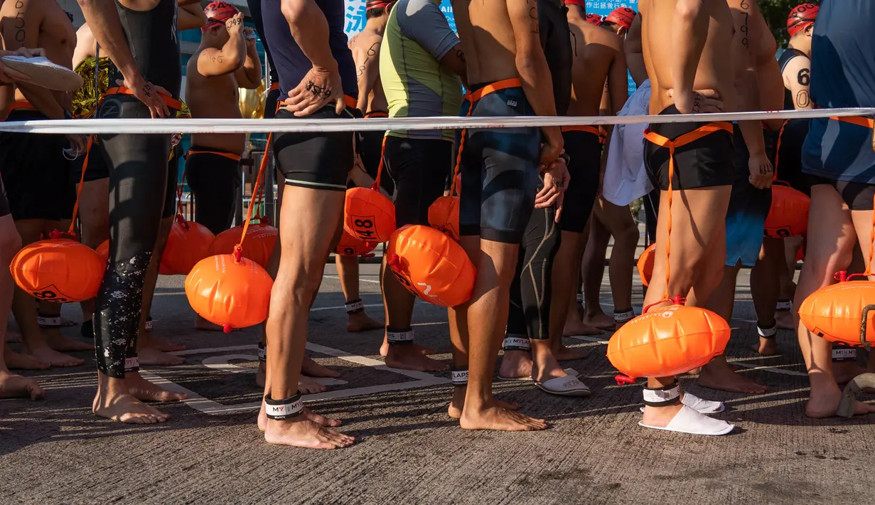 Perenang menunggu di garis start saat lomba renang tahunan melintasi Pelabuhan Victoria Hong Kong, Minggu (12/12/2021). Lomba renang tahunan itu diadakan untuk pertama kalinya dalam tiga tahun, setelah dibatalkan karena aksi demonstrasi besar-besaran dan kemudian pandemi COVID-19. (Bertha WANG/AFP)
