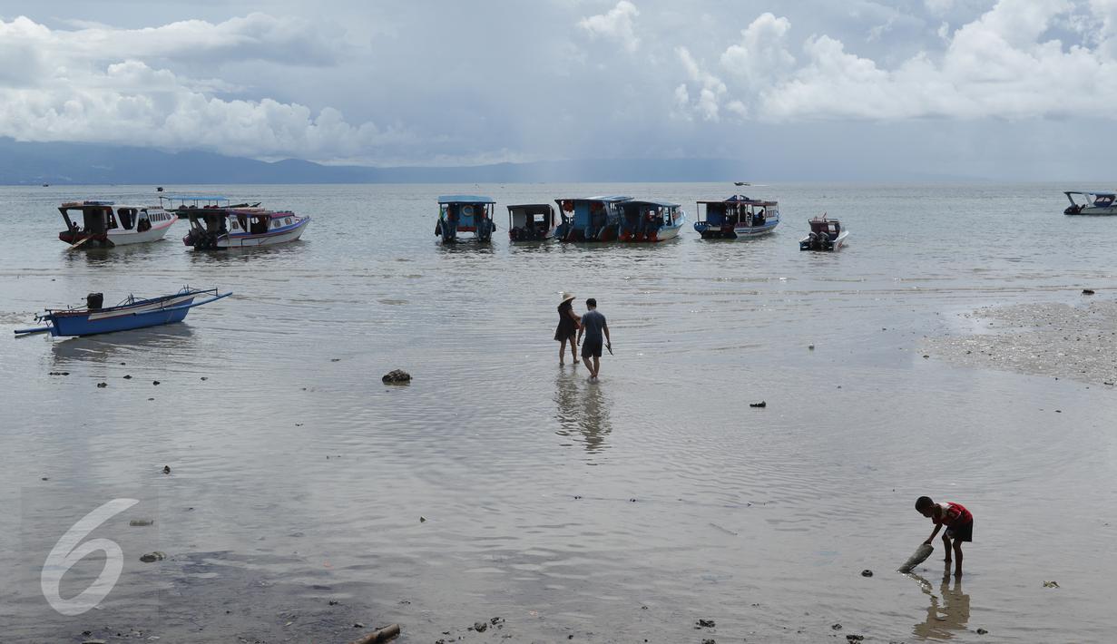 Sepasang wisatawan berjalan menuju kapal penumpang sementara seorang anak (kanan) bermain di pinggir pantai Pulau Bunaken, Manado, Sabtu (17/12). Taman Nasional Bunaken ini memiliki keindahan alam dan biota laut. (Liputan6.com/Fery Pradolo)