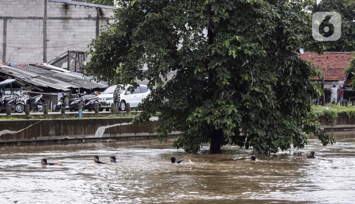 Anak-anak berenang di Sungai Ciliwung saat banjir melanda Jalan Bina Warga Rt 005/Rw 07 Kelurahan Rawa Jati, Jakarta, Senin (8/2/2021). Banjir setinggi 60-190 cm tersebut disebabkan oleh luapan air Sungai Ciliwung dan curah hujan Jakarta yang tinggi. (Liputan6.com/Johan Tallo)