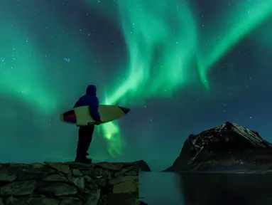 Seorang surfer melihat Cahaya Utara atau aurora borealis di Utakleiv, Norwegia utara (9/3). Aurora ini adalah sebuah peristiwa langit yang cantik berupa pancaran cahaya yang menyala-nyala di atmosfer sekitar lingkaran Arktik. (AFP/Olivier Morin)