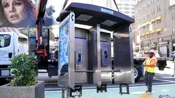 Para pekerja memindahkan bilik telepon umum terakhir NYC di dekat Seventh Avenue dan 50th Street di Midtown Manhattan, New York City, pada 23 Mei 2022. Telepon umum mulai menghilang dari jalan-jalan di New York pada awal 2000-an saat penggunaan telepon selular menyebar, dan kemudian menghilang lebih cepat pada 2010-an saat terjadi booming telepon pintar. (TIMOTHY A. CLARY / AFP)