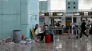 Penumpang memainkan ponsel di antara sampah yang berserakan di Bandara Barcelona, Spanyol, Kamis (1/12). Para petugas kebersihan melakukan aksi protes mengotori ruangan bandara dengan sampah sobekan kertas. (REUTERS/Albert Gea)