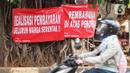 Pengendara motor melintas di depan poster protes warga terhadap pembangunan flyover di kawasan Tanjung Barat, Jakarta, Rabu (15/7/2020). Dalam poster protes tersebut, warga menuntut agar pembayaran pelunasan pembebasan lahan segera diselesaikan secara serentak. (Liputan6.com/Immanuel Antonius)