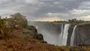 Seorang turis melihat Air Terjun Victoria yang megah di Zimbabwe (13/11/2019). Serangkaian gelombang panas telah mengeringkan sebagian besar vegetasi di sekitar situs warisan dunia UNESCO berukuran 108 meter dan lebar hampir 2 km dalam kekeringan parah. (AFP/Zinyange Auntony)