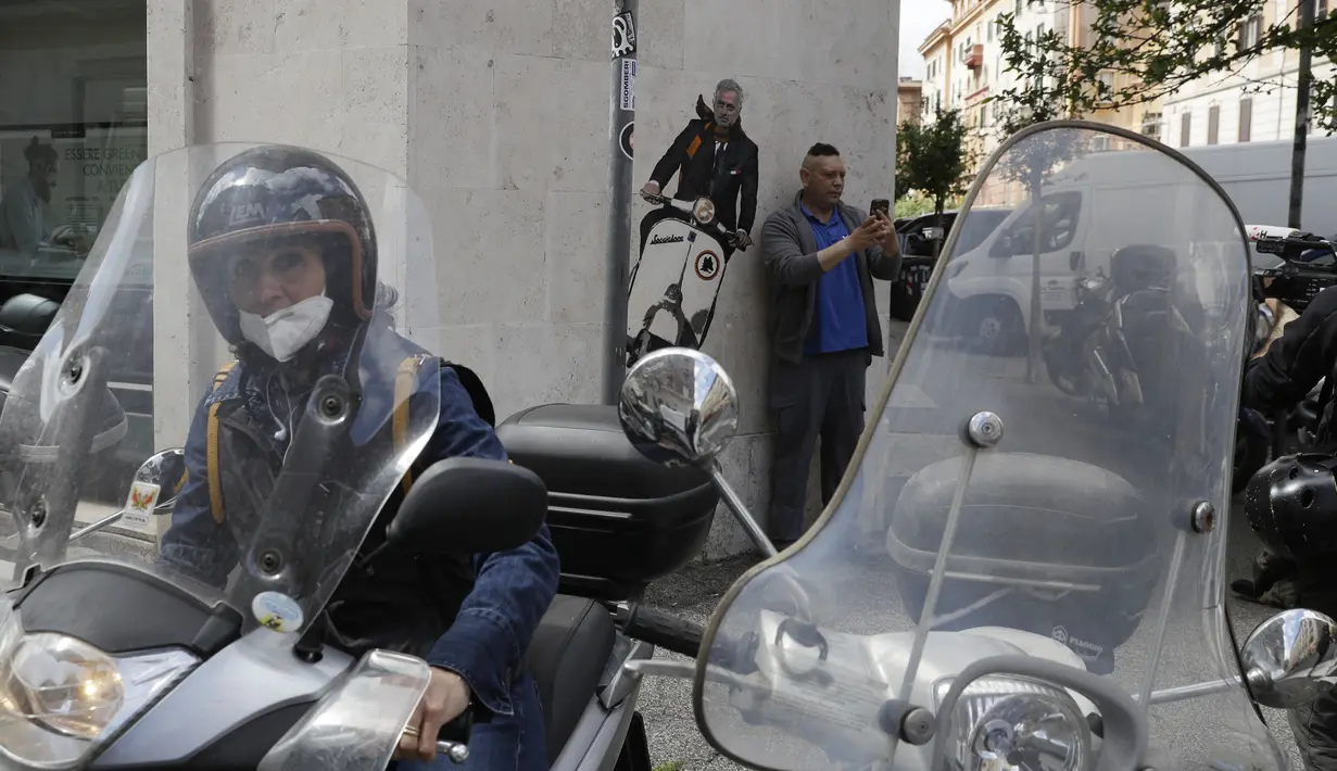 Seorang pria berselfie di dekat mural pelatih Jose Mourinho mengendarai skuter Vespa berhias lambang AS Roma di lingkungan Testaccio,  Roma (7/5/2021). Jose Mourinho dipecat Tottenham Hotspur pada 19 April kemarin. (AP Photo/Gregorio Borgia)