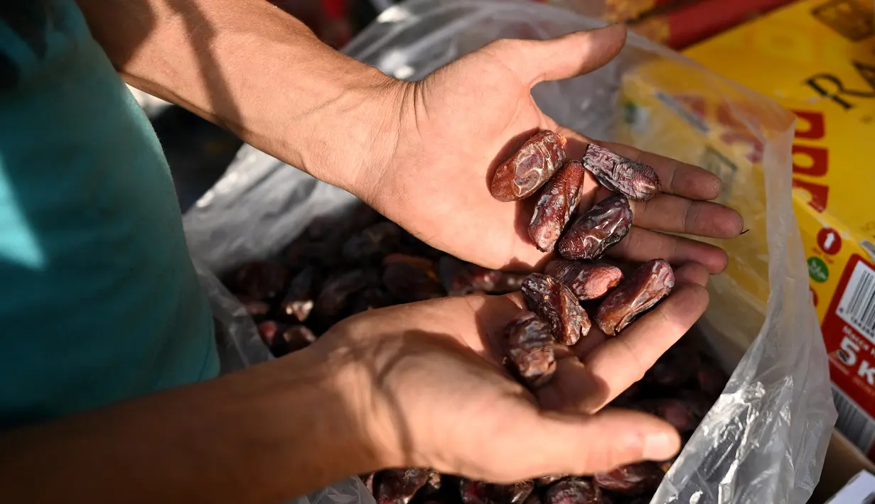 Pedagang memperlihatkan kurma dagangannya di sepanjang jalan menjelang bulan suci Ramadhan di Delhi, India pada Selasa (13/4/2021). Kurma sangat identik dengan bulan Ramadhan, karena buah yang satu ini kerap dijadikan pengisi menu sahur dan berbuka puasa. (Sajjad HUSSAIN / AFP)