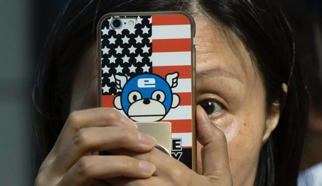 Seorang perempuan mengambil gambar dengan telepon yang memiliki sampul bertema bendera Amerika Serikat  di luar Konsulat Amerika Serikat di Chengdu, China barat daya pada 26 Juli 2020. (AP Photo / Ng Han Guan)