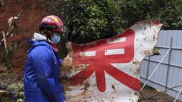 Seorang anggota tim penyelamat membawa potongan puing di lokasi kecelakaan penerbangan China Eastern di Kabupaten Tengxian di Daerah Otonomi Guangxi Zhuang, China selatan (24/3/2022). (Lu Boan/Xinhua via AP)