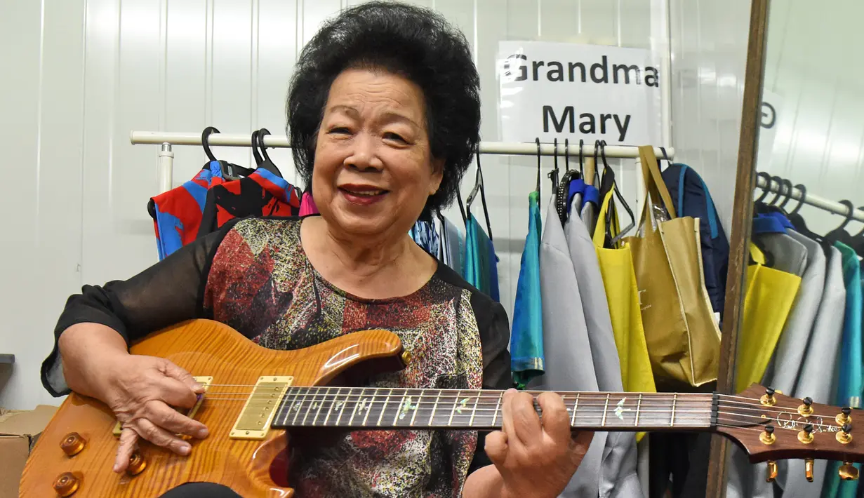 Mary Ho (81) berpose dengan gitar elektriknya saat melakukan latihan di Singapura, 5 Agustus 2017. Wanita yang dikenal sebagai Nenek Maria itu baru belajar gitar pada usia 60 tahun setelah sejak lama memimpikan belajar alat musik ini. (Roslan RAHMAN/AFP)
