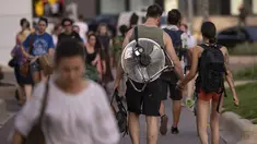 Seorang gadis berjalan bergandengan tangan dengan seorang pria yang membawa kipas angin di punggungnya pada malam yang panas di Bukares, Rumania, Selasa, 25 Juli 2023.  Suhu di tempat teduh mencapai di atas 40 derajat Celcius (104 Fahrenheit) di ibu kota Rumania, menurut layanan cuaca nasional karena gelombang panas terus mempengaruhi bagian selatan negara itu. (AP Photo/Andreea Alexandru)