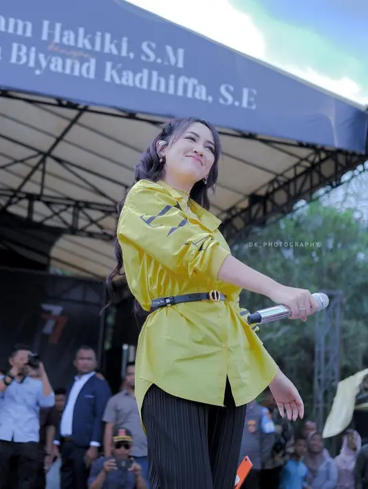 Gaya manggung simpel chic dari Happy Asmara. Ia mengenakan kemeja kuning lengan panjang dipadunya mengenakan celana panjang hitam dan belt kecil berwarna hitam yang manis. [Foto: Instagram/happy_asmara77]