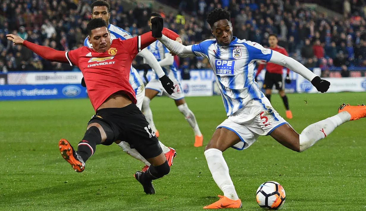 Bek Manchester United Chris Smalling berebut bola dengan pemain Huddersfield Town, Terence Kongolo pada pertandingan putaran kelima Piala FA di John Smith's Stadium, Minggu (18/2). MU melaju ke perempatfinal Piala FA setelah menang 2-0. (Oli SCARFF/AFP)