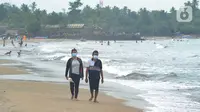 Wisatawan yang mengenakan masker menikmati suasana Pantai Anyer di Cilegon, Banten, Minggu (25/10/2020). Akhir pekan dimanfaatkan warga Jakarta dan sekitarnya untuk berwisata dengan tetap menerapkan protokol kesehatan Covid-19. (merdeka.com/Arie Basuki)