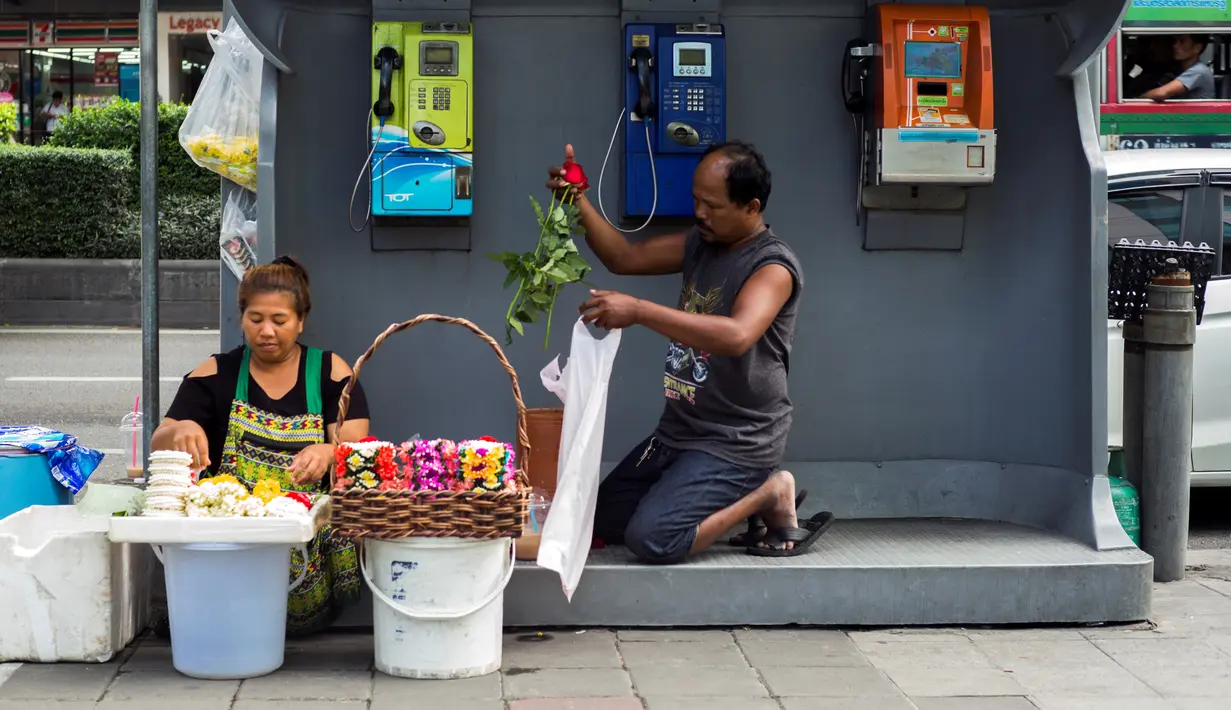 Dua pedagang menyiapkan bunga dagangannya di bilik telepon umum di samping jalan di Bangkok, Thailand (20/9). (AFP Photo/Jewel Samad)