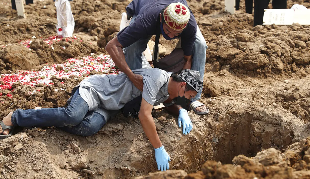 Seorang pria jatuh ke tanah saat dia menangis selama pemakaman kerabat yang meninggal karena COVID-19 di TPU Rorotan, Jakarta, Rabu (7/7/2021). Indonesia menghadapi gelombang kedua COVID-19. (AP Photo/Tatan Syuflana)