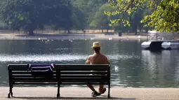 Seorang pria duduk di bangku menikmati suasana sungai Serpentine di Hyde Park di London, Rabu, (12/8/2020). Peringatan badai masih berlaku untuk sebagian besar Inggris pada hari Rabu, sementara suhu tinggi diperkirakan lagi di banyak bagian Inggris. ( AP Photo / Kirsty Wigglesworth)