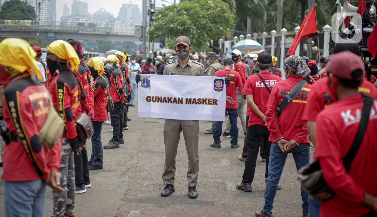 Petugas Satpol PP memegang poster imbauan protokol kesehatan COVID-19 saat unjuk rasa buruh di depan Gedung DPR, Jakarta, Selasa (17/11/2020). Pemerintah terus mengingatkan pentingnya 3M yaitu memakai masker, menjaga jarak, dan mencuci sebagai upaya pencegahan Covid-19. (Liputan6.com/Faizal Fanani)