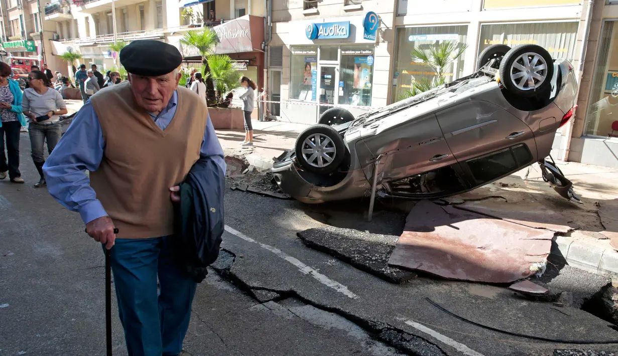 Seorang pria berjalan melewati mobil yang terbalik dan jalanan yang hancur akibat banjir di Cannes, Prancis, Minggu (4/10/2015). Akibat peristiwa itu, sebanyak 16 warga dilaporkan tewas. (REUTERS/Eric Gaillard)