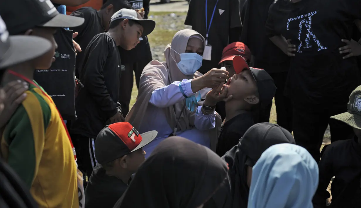 Seorang anak lak-laki menerima imunisasi polio dari petugas medis saat berlangsung vaksinasi massal di Sigli Town Square,  Pidie, Aceh, Senin (28/11/2022). Kementerian Kesehatan melakukan vaksinasi massal sebanyak 1.000 anak dari target target 9.940 anak. (AP Photo/Riska Munawarah)