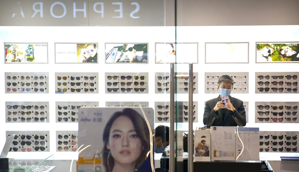 Seorang pegawai mengenakan masker menggunakan smartphone-nya ketika ia menunggu pelanggan di toko kacamata di pusat perbelanjaan di Beijing (28/1/2020).  Hingga Rabu (5/2/2020) pagi, jumlah pasien yang meninggal menjadi 479. (AP Photo/Mark Schiefelbein)