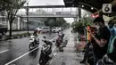 Pejalan kaki dan pengendara motor berteduh saat hujan di Jalan Pramuka, Jakarta, Kamis (18/2/2021). BMKG mengimbau pengguna jalan agar berhati-hati saat berkendara karena musim hujan disertai angin kencang diprediksi terus berlanjut hingga akhir Februari. (merdeka.com/Iqbal S Nugroho)