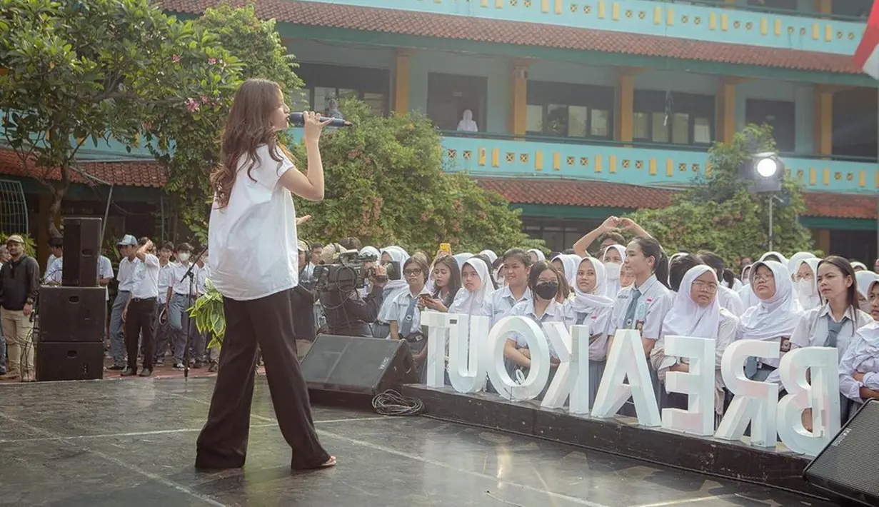 Anggi Marito membagikan potret keseruannya saat tampil bernyanyi di SMAN 47 Jakarta. Perempuan kelahiran 6 Maret 2002 itu tampil kasual dengan kemeja putih dan celana panjang hitam. Para pelajar tampak ikut bernyanyi bareng Anggi yang memukau di atas panggung. (Liputan6.com/IG/@anggimarito)