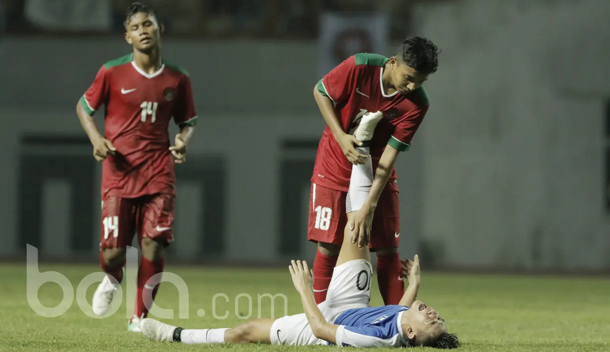 Pemain Timnas Indonesia U-16, Fadilah Nur Rahman, membantu pemain Singapura, Marc Ryan yang cidera pada laga uji coba Internasional di Stadion Wibawa Mukti, Cikarang, Kamis, (8/6/2017). Indonesia menang 4-0. (Bola.com/M Iqbal Ichsan)