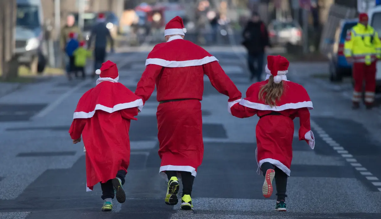 Seorang pria bersama dua anak berkostum Santa Claus ikut dalam kegiatan  Santa Claus Run di Michendorf, Minggu (10/12). Kegiatan amal yang digelar setiap tahun ini diikuti ribuan warga Jerman dan wisatawan mancanegara. (Ralf Hirschberger / dpa / AFP)