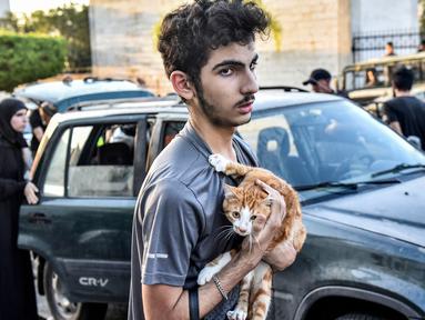 Seorang pemuda memeluk seekor kucing di dadanya saat orang-orang yang melarikan diri dari desa mereka di Lebanon selatan diterima di sebuah lembaga seni yang diubah menjadi tempat penampungan bagi para pengungsi akibat konflik, di Beirut pada 23 September 2024. (FADEL ITANI/AFP)
