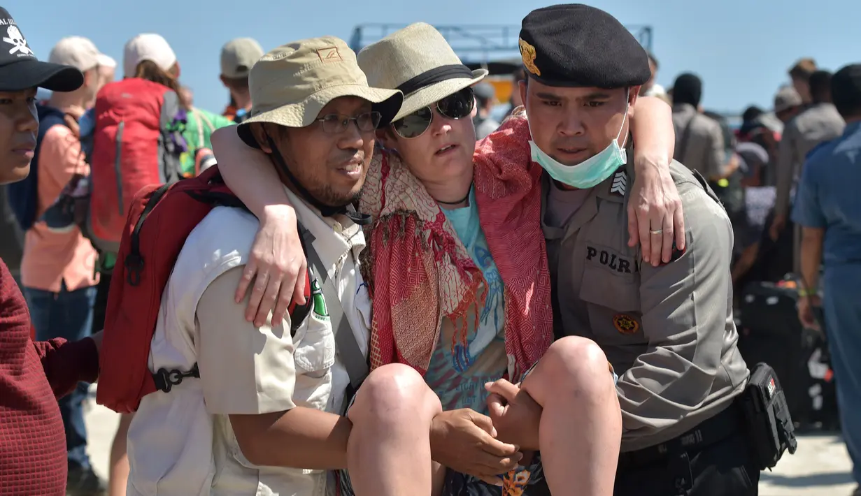 Petugas kepolisian dan penyelamat membantu turis asing yang dievakuasi dari Gili Trawangan saat tiba di Pelabuhan Bangsal, Lombok Utara, NTB, Selasa (7/8). Ribuan turis asing dievakuasi dari Gili Trawangan setelah gempa Lombok. (ADEK BERRY/AFP)