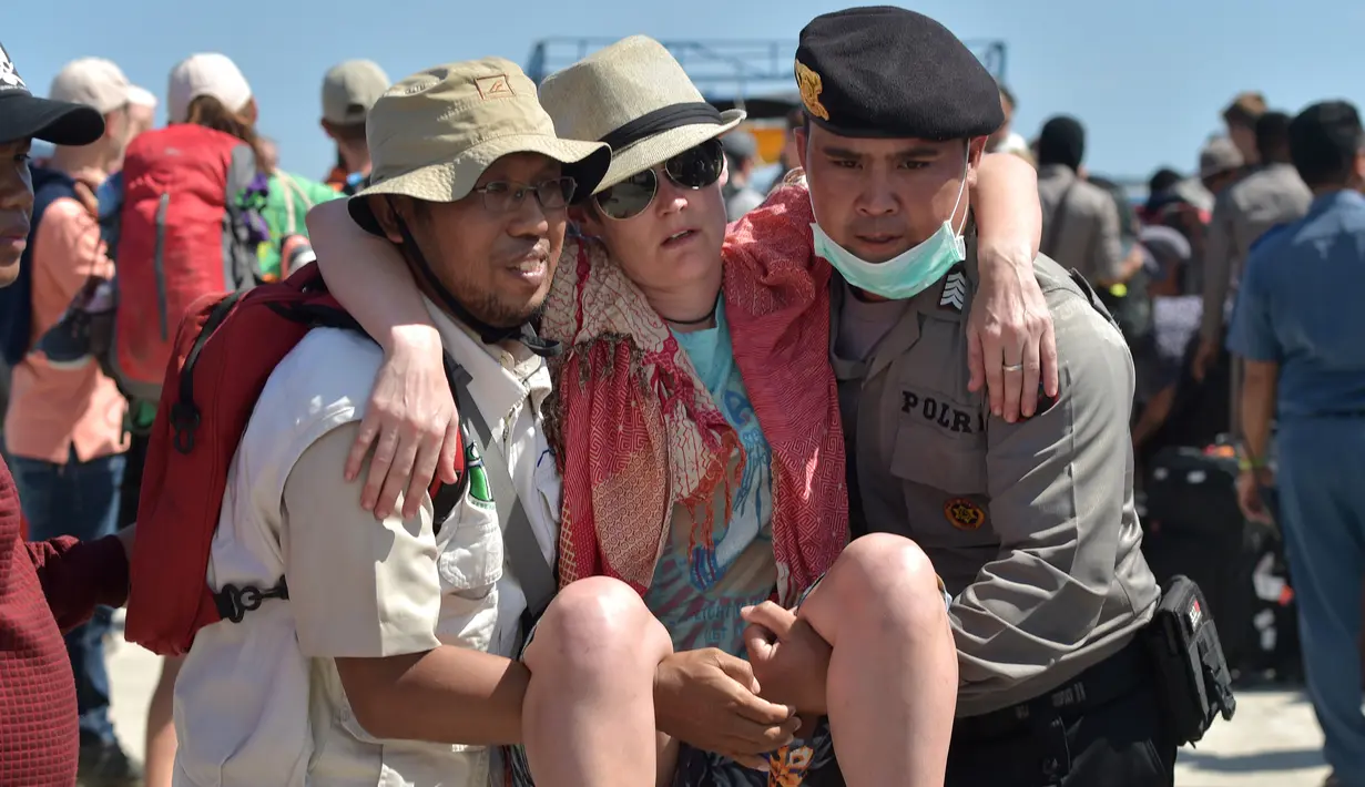 Petugas kepolisian dan penyelamat membantu turis asing yang dievakuasi dari Gili Trawangan saat tiba di Pelabuhan Bangsal, Lombok Utara, NTB, Selasa (7/8). Ribuan turis asing dievakuasi dari Gili Trawangan setelah gempa Lombok. (ADEK BERRY/AFP)