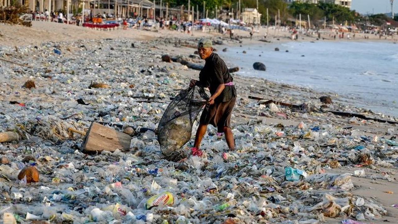 Seorang warga mengumpulkan sampah di Pantai Kedonganan, Kuta, Badung, Bali, Selasa (19/3/2024). Sampah kiriman yang terbawa ombak di lautan itu tampak menutupi hamparan pasir putih di Pantai Kedonganan.&nbsp;Sonny Tumbelaka/AFP