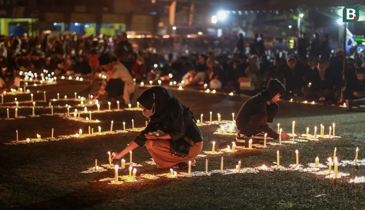 Di bagian tengah lapangan, lilin yang dibentuk tulisan Arema tetap diupayakan hidup. Jika ada yang mati, aremania yang ada di dekatnya bergegas menyalakannya dengan korek api. (Bola.com/Bagaskara Lazuardi)
